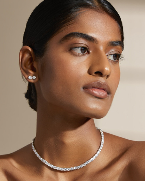 A woman wearing a natural diamond necklace and diamond stud earrings