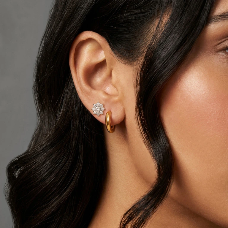 Elegant close‑up portrait on ear featuring a woman with elegant hair. She has indian features. She is wearing a single small gold hoop earring with. Soft, warm studio lighting and a neutral, minimal background. High‑end jewelry editorial style, clean composition, high‑resolution fashion photography.