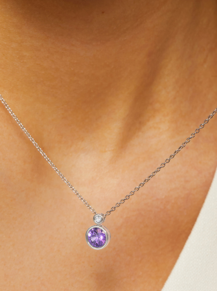 Close up of an amethyst and diamond pendant on a silver chain
