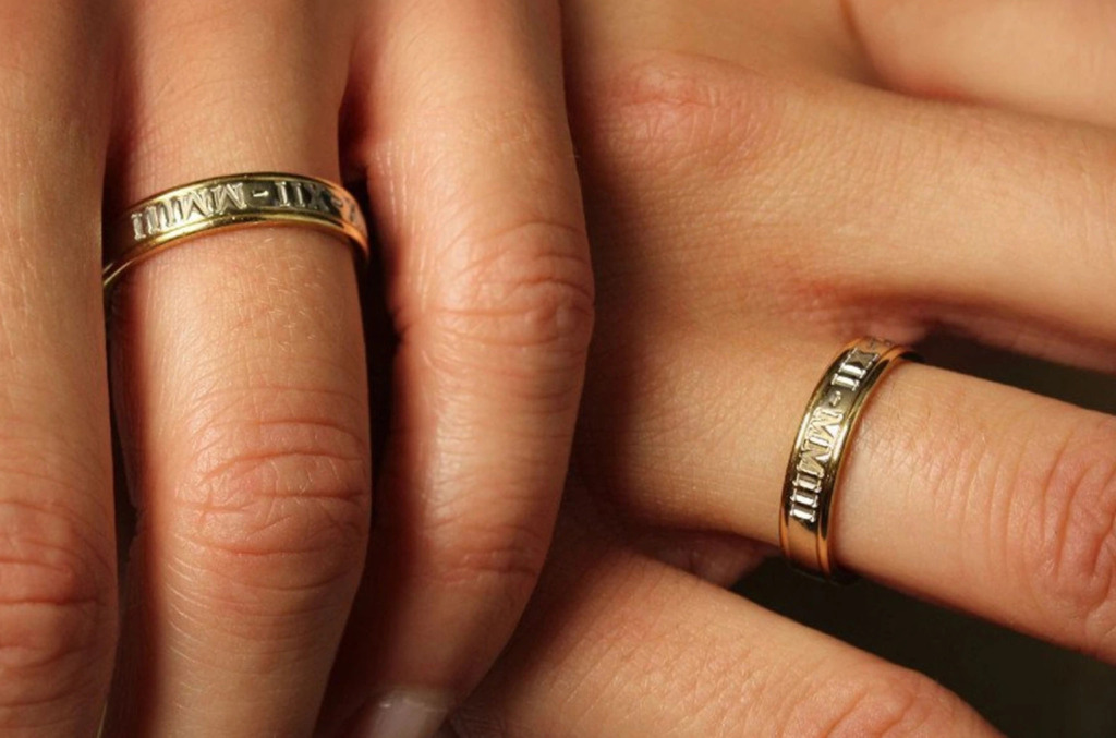 Close up of two hands wearing engraved wedding bands