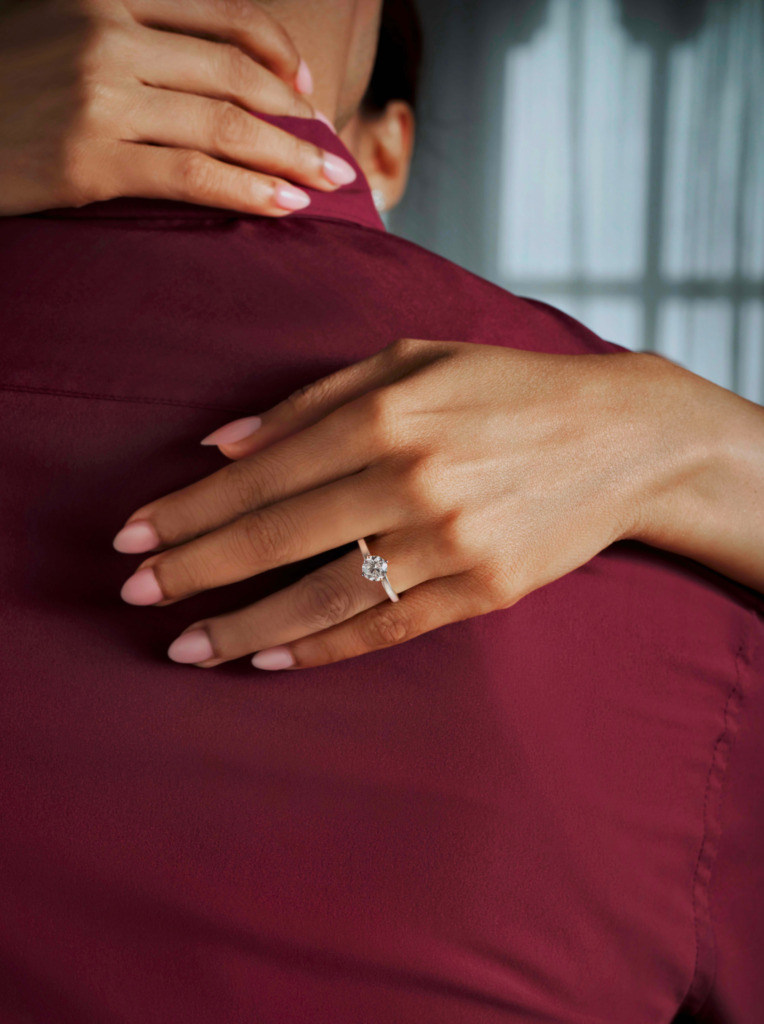 A woman's hand on her partner's back, adorned with a natural diamond solitaire ring