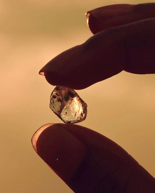 Fingers holding a natural rough diamond