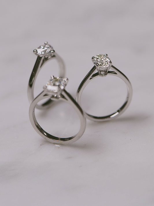 Set of three solitaire diamond engagement rings on grey background