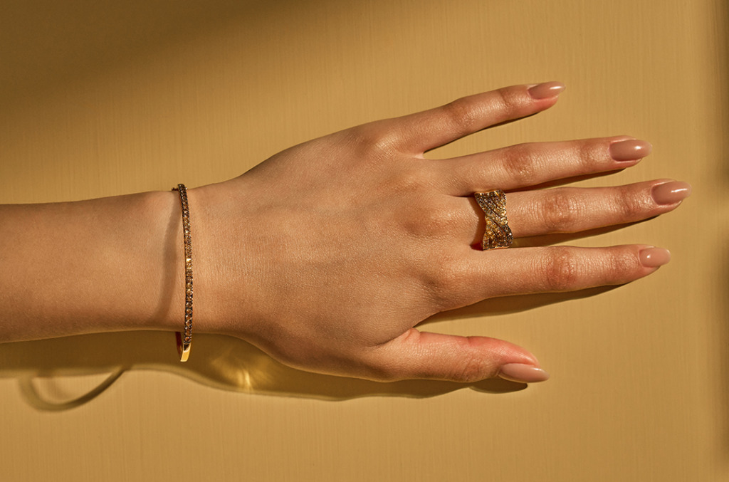 White hand on gold background wearing desert diamond bangle and ring