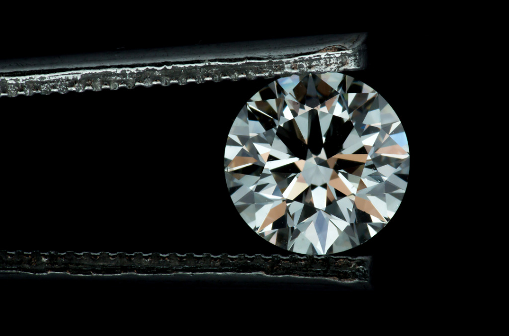 A round brilliant-cut diamond held by metal tweezers against a black background, its facets reflecting light after professional cleaning.