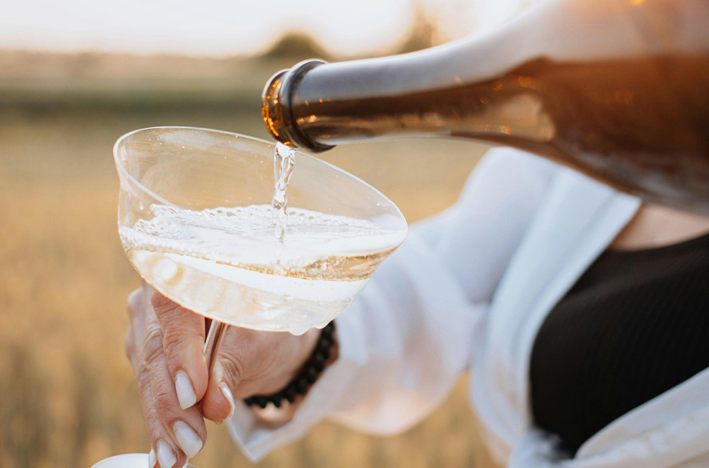 Close-up of champagne being poured into a coupe glass outdoors, the golden bubbles catching the light in tones reminiscent of Champagne Desert diamonds.