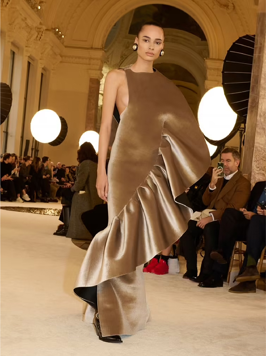 Model walking the runway at Schiaparelli’s Spring/Summer 2025 show wearing sculptural gown in champagne and golden-beige tones, echoing the luminous warmth of Champagne diamonds.