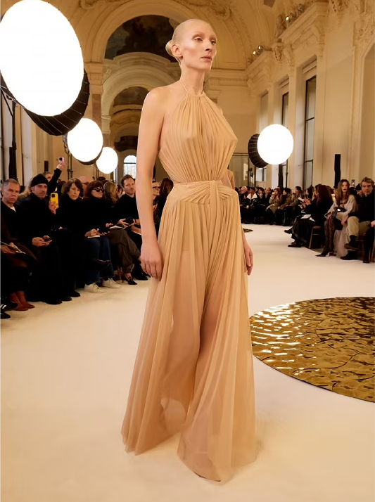 Model walking the runway at Schiaparelli’s Spring/Summer 2025 show wearing sculptural gown in champagne and golden-beige tones, echoing the luminous warmth of Champagne diamonds.