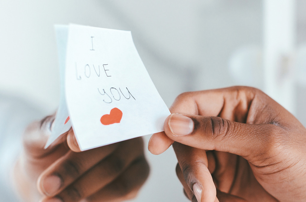 A close-up of a person holding a handwritten note that reads “I love you” with a small red heart.