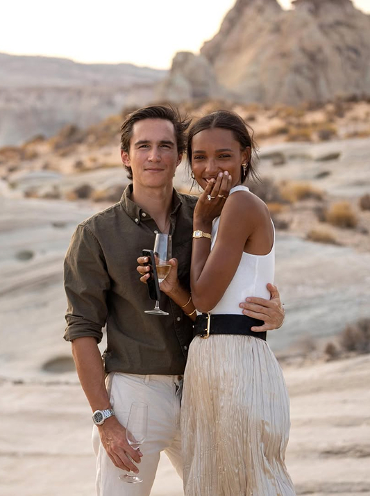 Jasmine Tookes and her fiancé standing together in the Utah desert, smiling and holding champagne after their engagement.