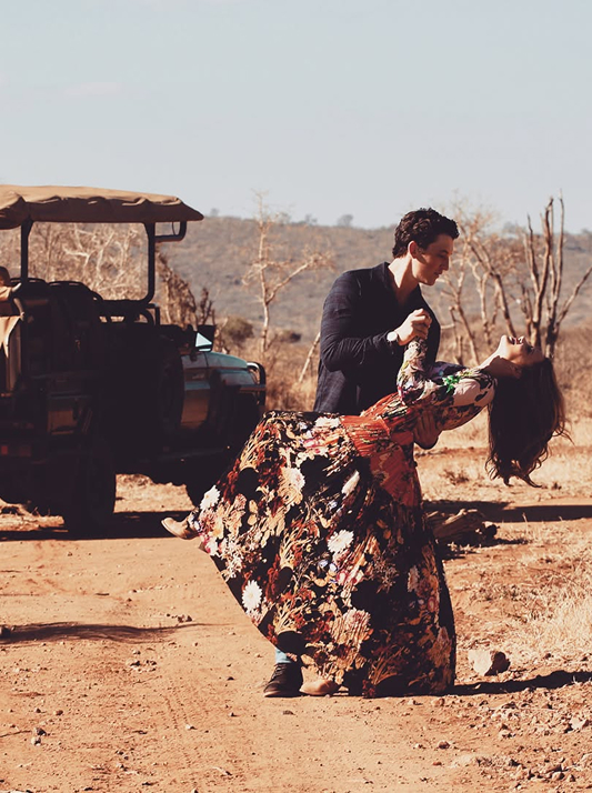 Miles Teller holding Keleigh Sperry in a dip beside a safari vehicle in South Africa.
