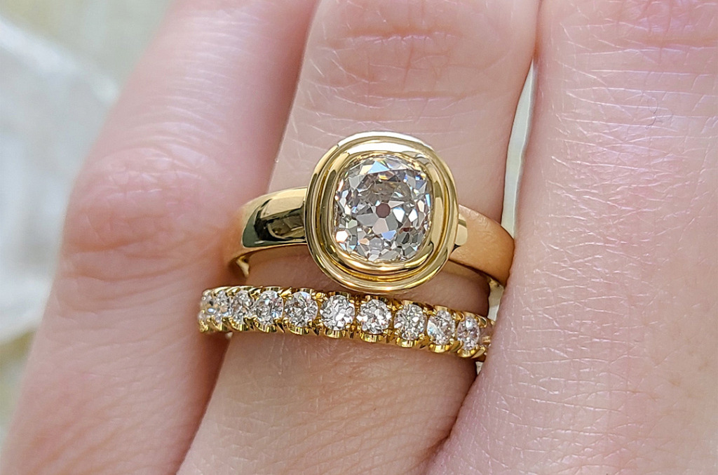 Cushion-cut natural diamond engagement ring in a yellow gold bezel setting, paired with a diamond pavé band, showcasing antique-inspired design and modern proportions.