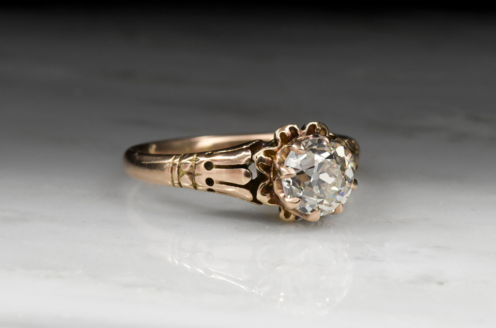 Close-up of a vintage Victorian engagement ring featuring intricate gold metalwork and a round natural diamond set in a floral-inspired bezel.