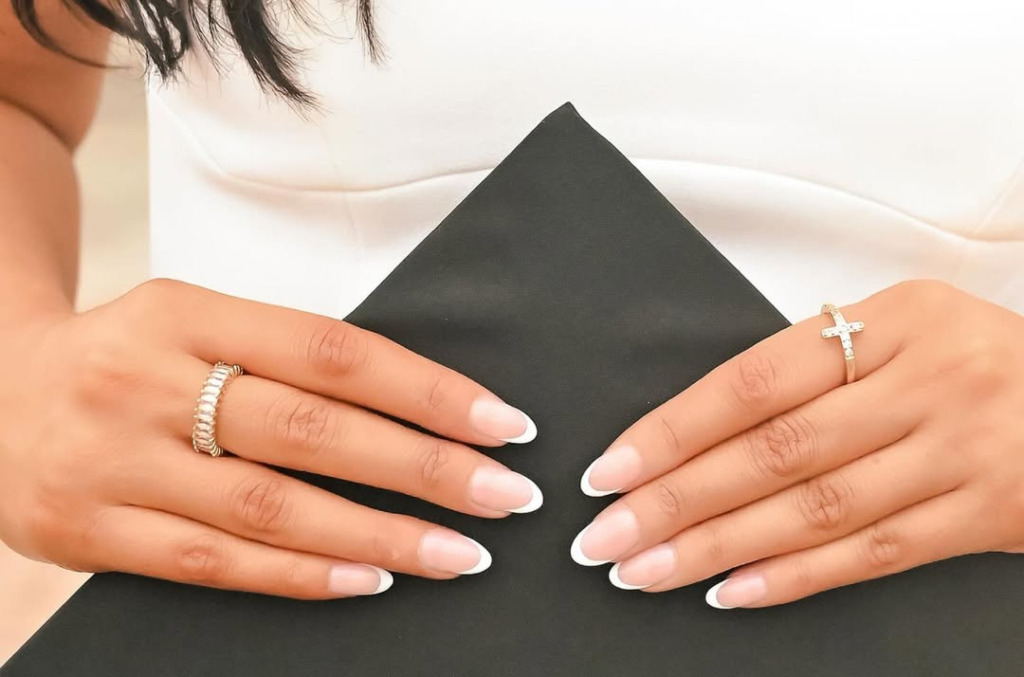 Close-up of a graduate’s hands holding a black graduation cap, wearing two delicate diamond rings.