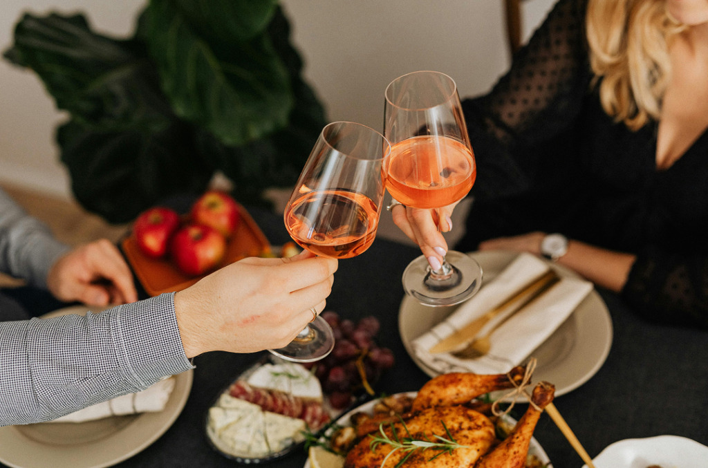 Close-up of a couple toasting with glasses of rosé over a home-cooked dinner, with a set table and warm, intimate lighting.