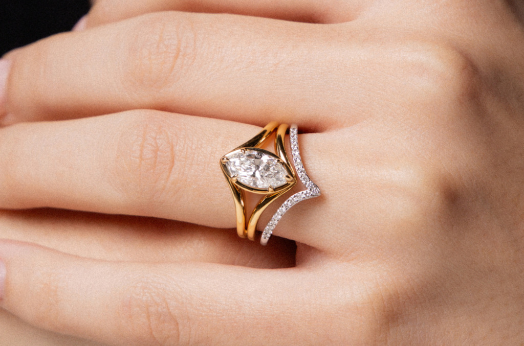Close-up of a hand wearing a custom-designed natural diamond ring with a sculptural gold setting and curved diamond-accented band.