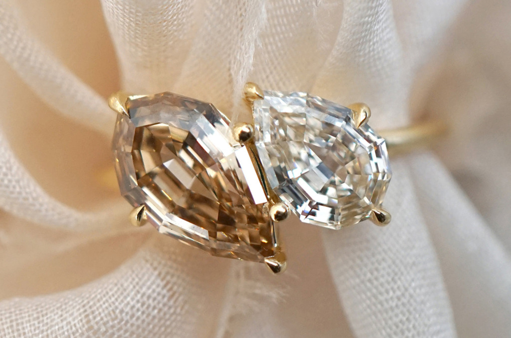Close-up of a toi et moi ring featuring two natural diamonds in contrasting shapes and tones, set side by side in yellow gold.