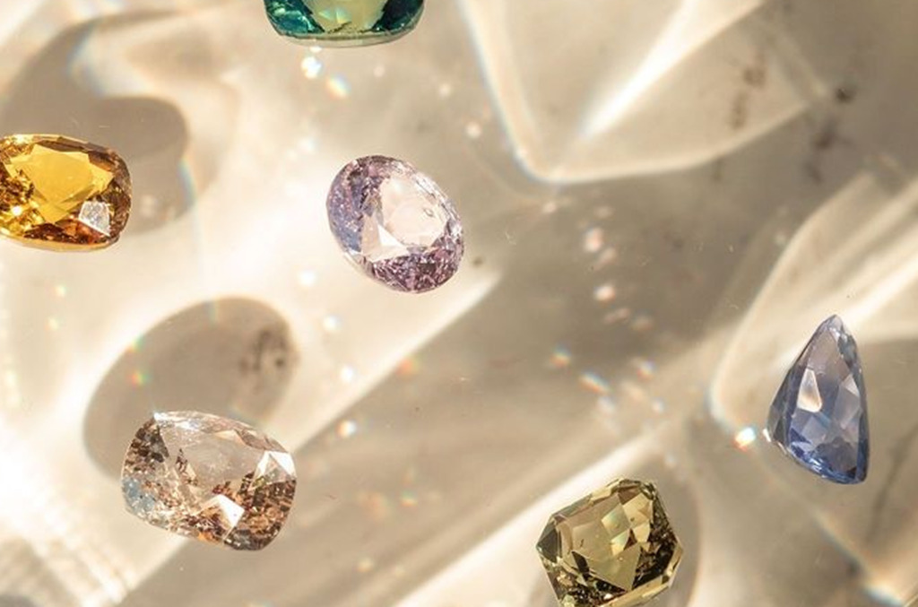 Loose natural diamonds in a range of colors, including yellow, pink, blue, and champagne tones, scattered across a softly lit surface.