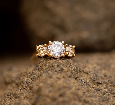 Gold ring with three round diamonds in champagne and white tones, displayed on textured brown rock.