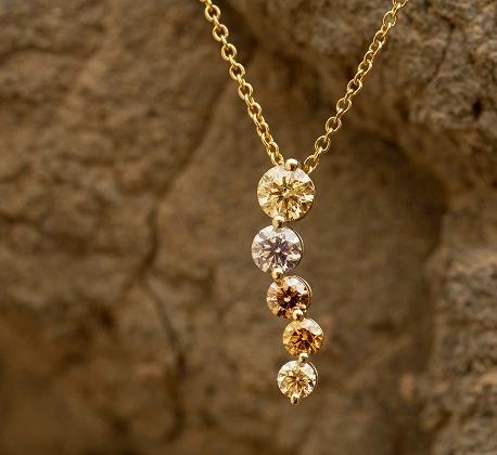 Gold necklace with five round diamonds in graduated champagne and white shades, photographed against a natural rock background.