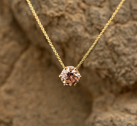 Gold necklace featuring a single round champagne diamond pendant, set against a rocky background.